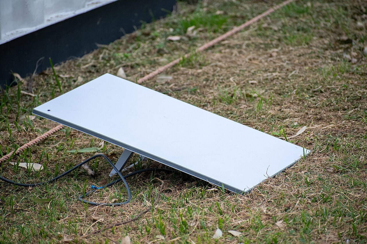 Flache Starlink-Antenne auf einer Wiese, ein Kabel führt zur Antenne