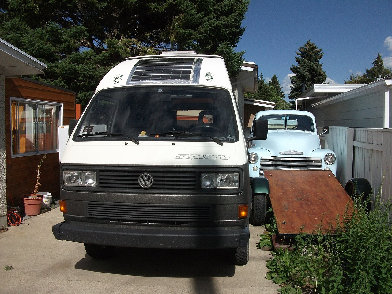 Weißer VW-Camper (T3 Syncro) mit Hochdach und einem aufgebauten Solarmodul auf dem Dach, von vorne fotografiert.